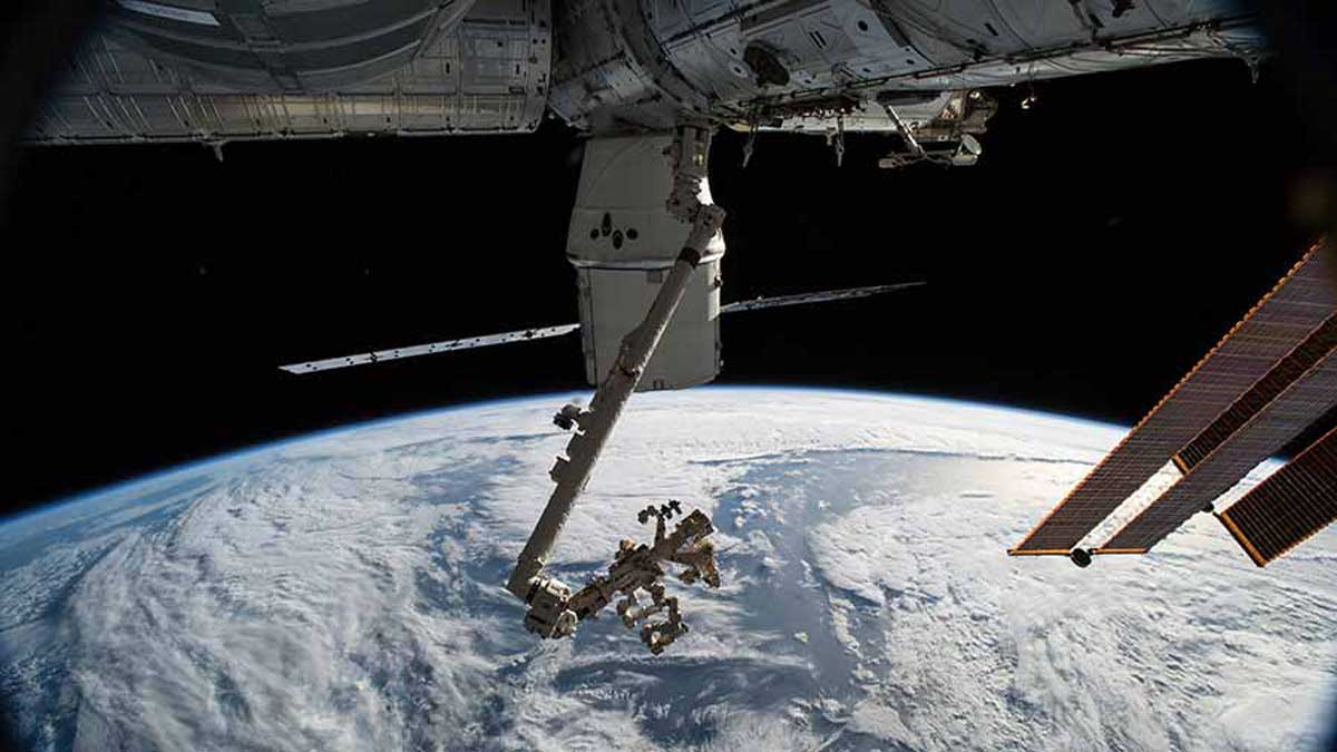 Le vaisseau de ravitaillement SpaceX Dragon et le bras robotique Canadarm2 avec le manipulateur adroit à usage spécial, Dextre, sont illustrés comme la station spatiale orbitant au-dessus du golfe d’Alaska.