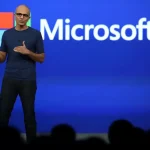 Satya Nadella sur scène lors d’une présentation Microsoft, devant un fond bleu avec le logo de l’entreprise