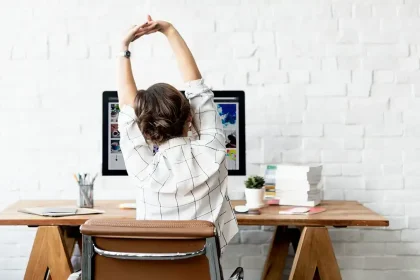 Une femme s'étire sur sa chaise de bureau devant son ordinateur, illustrant l'importance d'une bonne posture pour le travail prolongé.