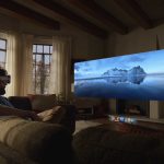 Un homme portant un casque Apple Vision Pro assis sur un canapé, regardant une projection immersive d'un paysage de montagne glacée.