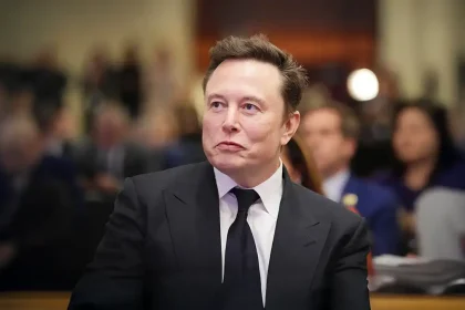 Portrait d'Elon Musk lors d'une conférence de presse, regard concentré vers la droite, en costume-cravate sombre.