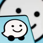 Logo de l’application Waze affiché sur un smartphone, avec un fond flou reprenant l’icône de l’application.