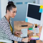 Graphiste concentrée utilisant une tablette graphique dans un bureau moderne, devant un grand écran.