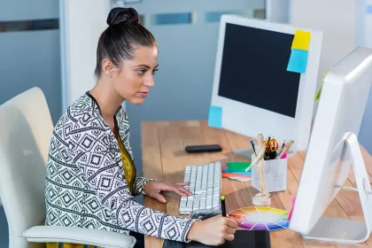 Graphiste concentrée utilisant une tablette graphique dans un bureau moderne, devant un grand écran.