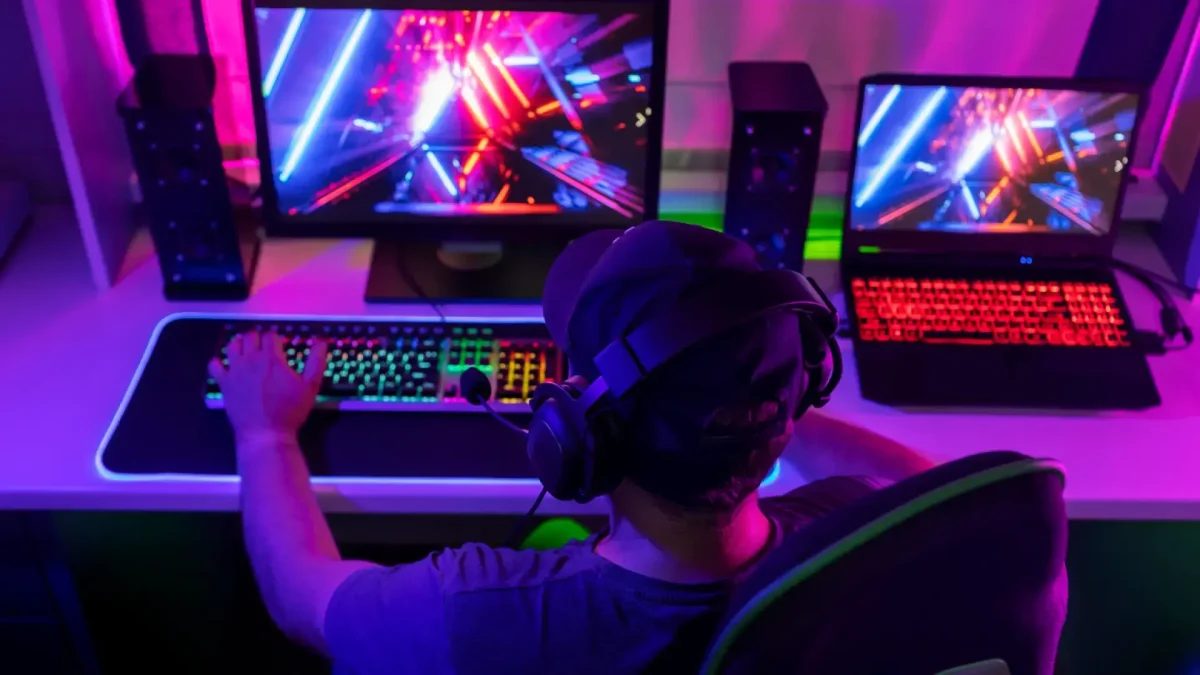 Joueur sur PC équipé d’un casque, en pleine session gaming avec affichage coloré sur deux écrans.