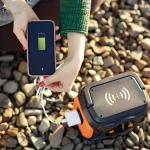 Femme rechargeant un smartphone via une batterie externe sur un sol en gravier