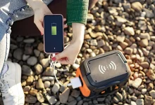 Femme rechargeant un smartphone via une batterie externe sur un sol en gravier