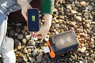 Femme rechargeant un smartphone via une batterie externe sur un sol en gravier