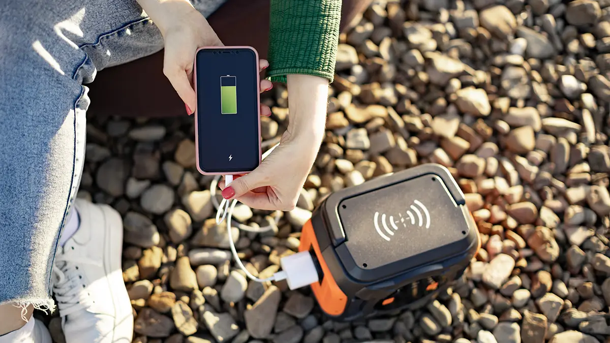 Femme rechargeant un smartphone via une batterie externe sur un sol en gravier