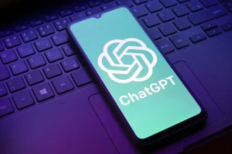 Smartphone affichant le logo ChatGPT posé sur le clavier d’un ordinateur portable, illustrant l’intégration de l’IA dans les usages numériques quotidiens.