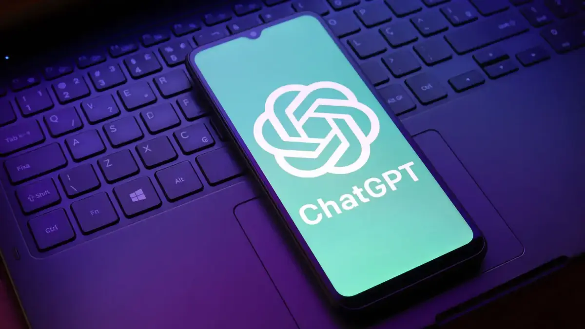 Smartphone affichant le logo ChatGPT posé sur le clavier d’un ordinateur portable, illustrant l’intégration de l’IA dans les usages numériques quotidiens.