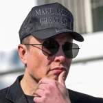 Elon Musk portant une casquette noire et des lunettes de soleil, pensif