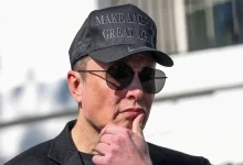 Elon Musk portant une casquette noire et des lunettes de soleil, pensif