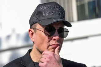 Elon Musk portant une casquette noire et des lunettes de soleil, pensif