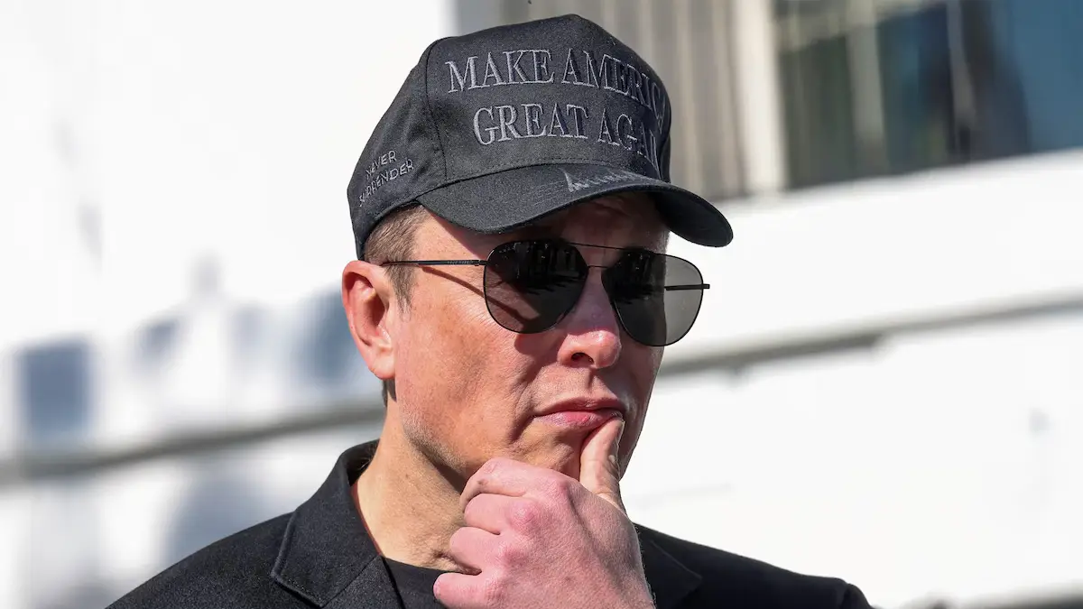 Elon Musk portant une casquette noire et des lunettes de soleil, pensif