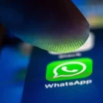 Icône WhatsApp sur smartphone sous un doigt, interface mobile en gros plan