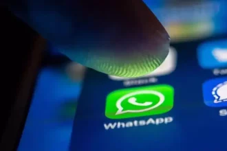 Icône WhatsApp sur smartphone sous un doigt, interface mobile en gros plan