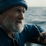 Vieil homme barbu en tenue de marin, fumant la pipe sur un bateau, face à la mer agitée