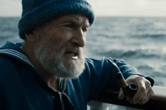 Vieil homme barbu en tenue de marin, fumant la pipe sur un bateau, face à la mer agitée