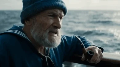 Vieil homme barbu en tenue de marin, fumant la pipe sur un bateau, face à la mer agitée