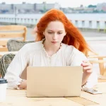 Femme concentrée devant son ordinateur portable dans un café en plein air, illustrant la vigilance face à la publicité ciblée