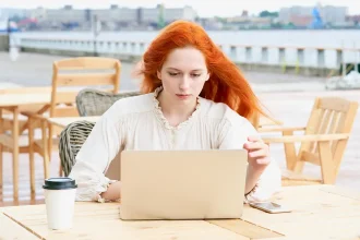 Femme concentrée devant son ordinateur portable dans un café en plein air, illustrant la vigilance face à la publicité ciblée