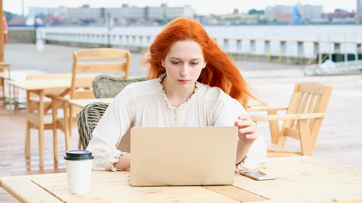 Femme concentrée devant son ordinateur portable dans un café en plein air, illustrant la vigilance face à la publicité ciblée