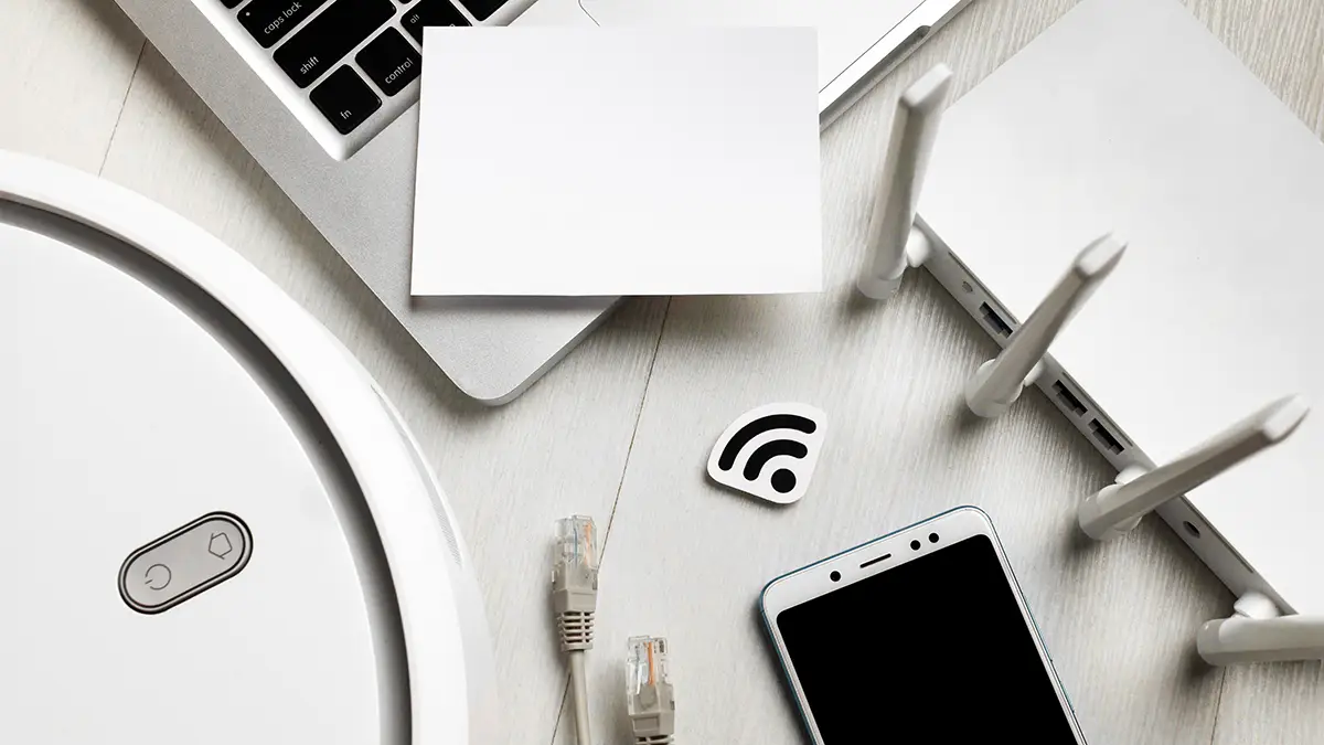 Vue de dessus d’un routeur Wi-Fi entouré d’appareils connectés, smartphone, câble réseau et robot aspirateur