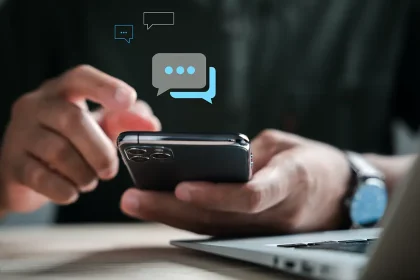 Main tenant un smartphone, écran affichant des bulles de messages SMS, devant un ordinateur portable