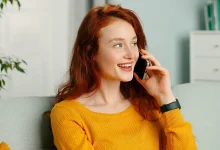 Jeune femme souriante assise sur un canapé, en train de téléphoner dans un intérieur lumineux