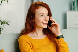 Jeune femme souriante assise sur un canapé, en train de téléphoner dans un intérieur lumineux