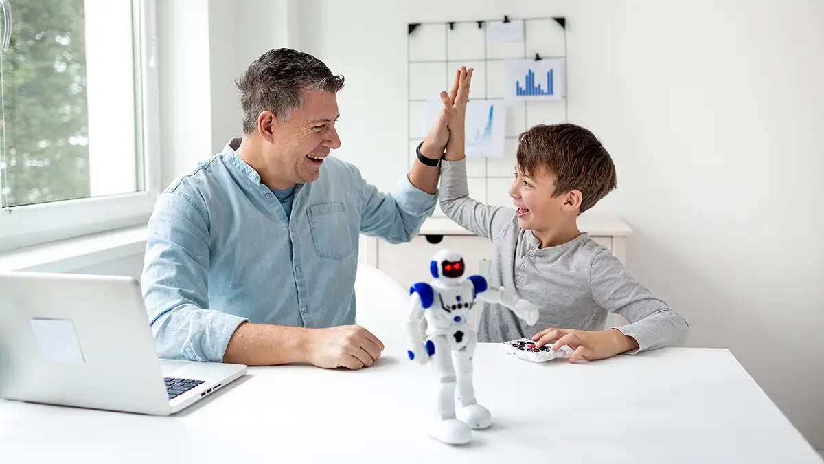 Un père et son fils sourient et se donnent un high five devant un robot interactif, symbole des nouveaux cadeaux fête des pères inspirés par l’intelligence artificielle.