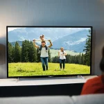 Personne sur un canapé devant une télévision allumée dans un salon sombre, lumière d’écran et lampes, habitude nocturne.