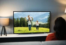 Personne sur un canapé devant une télévision allumée dans un salon sombre, lumière d’écran et lampes, habitude nocturne.