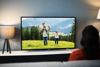 Personne sur un canapé devant une télévision allumée dans un salon sombre, lumière d’écran et lampes, habitude nocturne.