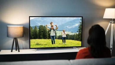 Personne sur un canapé devant une télévision allumée dans un salon sombre, lumière d’écran et lampes, habitude nocturne.