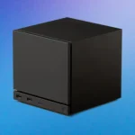 Mini-PC noir cubique rappelant une Steam Machine, posé sur fond bleu.