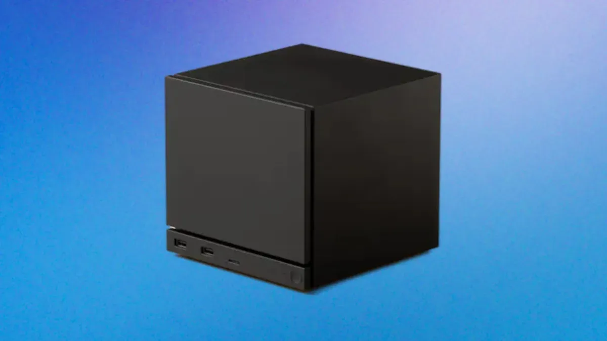 Mini-PC noir cubique rappelant une Steam Machine, posé sur fond bleu.