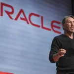 Larry Ellison s'exprimant au micro sur scène avec le logo Oracle affiché en grand en arrière-plan