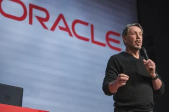 Larry Ellison s'exprimant au micro sur scène avec le logo Oracle affiché en grand en arrière-plan