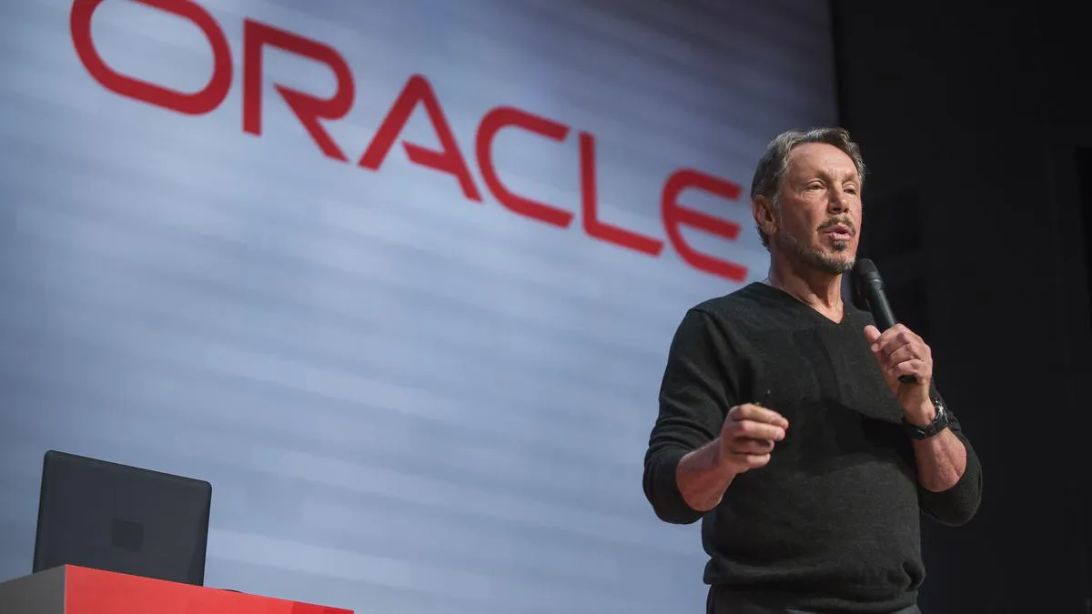 Larry Ellison s'exprimant au micro sur scène avec le logo Oracle affiché en grand en arrière-plan